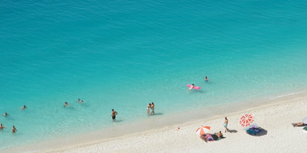 Mensen zwemmen in helder turquoise water bij een zandstrand